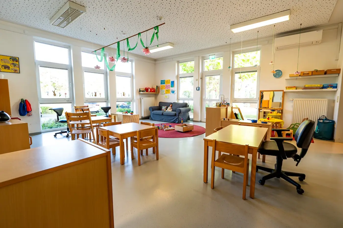 Heller Gruppenraum der Gruppe 1 mit blauem Sofa, Kindertischen und Spielteppich in der Kita Schweich