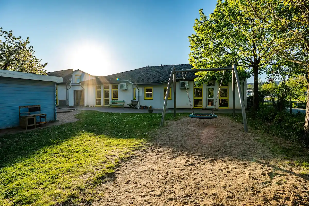 Außenansicht der Kita Schweich mit Sandkasten, Nestschaukel und großem Außengelände